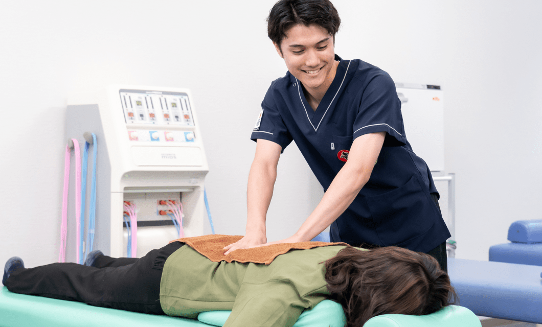 紺色の医療ユニフォームを着た施術者が、うつ伏せの患者の背中に両手で圧を加えている