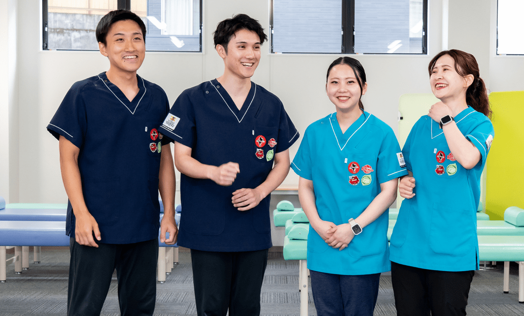 医療ユニフォームを着た4人のスタッフが室内で並び、笑顔で交流している様子