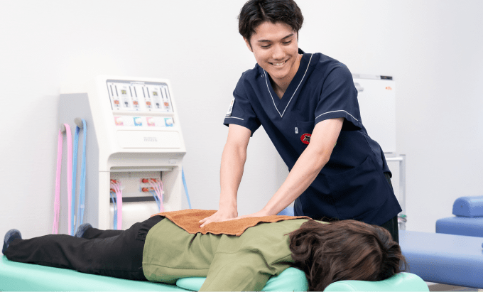 紺色の医療ユニフォームを着た施術者が、うつ伏せの患者の背中に両手で圧を加えている