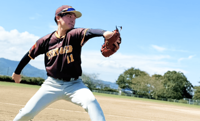 マルーン色のユニフォーム姿の投手が右腕を大きく振りかぶり、ボールを投げる瞬間