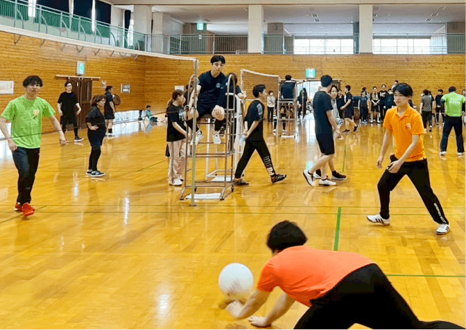 体育館で行われる活気あるバレーボールの試合、オレンジ色のユニフォームの選手がダイブしてボールを返そうとしている