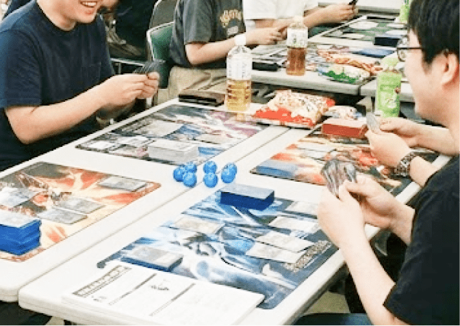 テーブルにカードやプレイマットを広げ、談笑しながらカードゲームを楽しむ人々の穏やかな時間