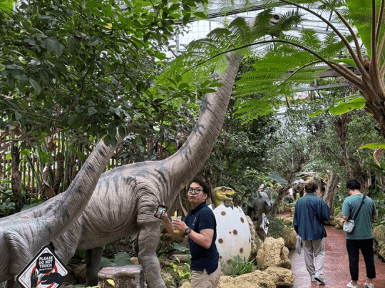 緑豊かなジャングル風の屋内展示で、リアルな恐竜模型と人々が楽しそうに過ごしている