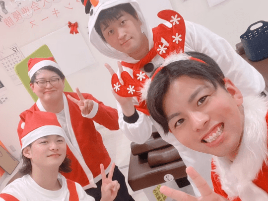クリスマスの仮装をした4人が笑顔で記念撮影し、祝祭的な雰囲気を伝えている