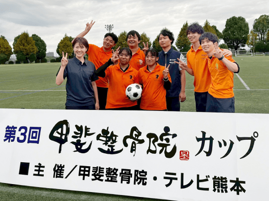 『第3回 甲斐整骨院カップ』と書かれたバナーの前で、8人が笑顔で記念撮影
