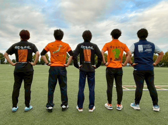 スポーツフィールドで背中を見せ、団結を示すように並ぶ5人